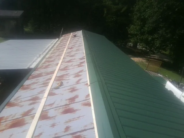 Old rusted panels beside newly installed green metal roofing — Wind Damage Roof Repair by Roofing Brothers in Everglades City