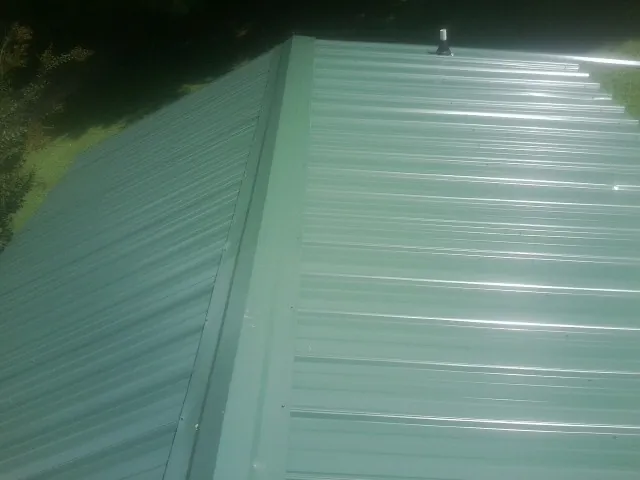 New green metal panels meeting at the ridge of a roof — Flat Roof Repair work by our crew in Everglades City